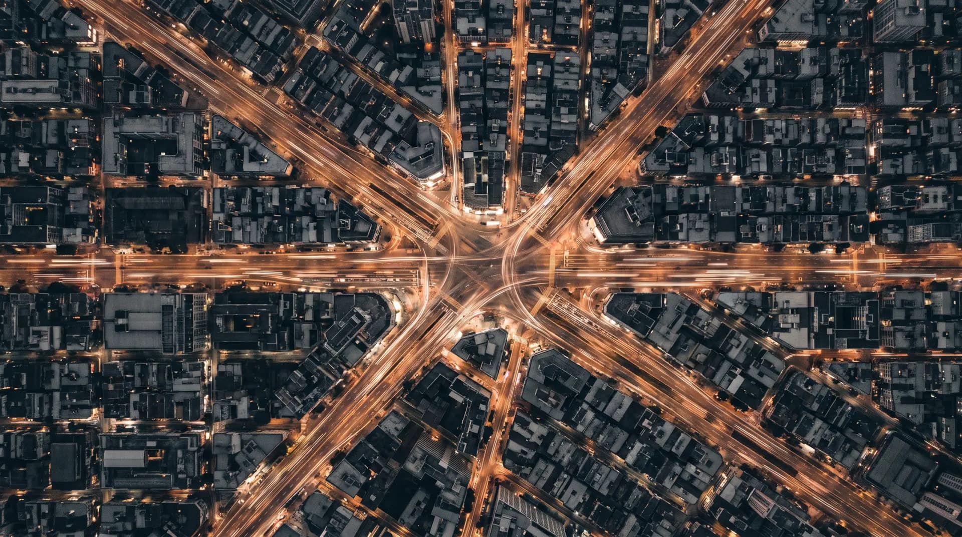 Aerial view of a city intersection at night, with traffic streaking along the roads